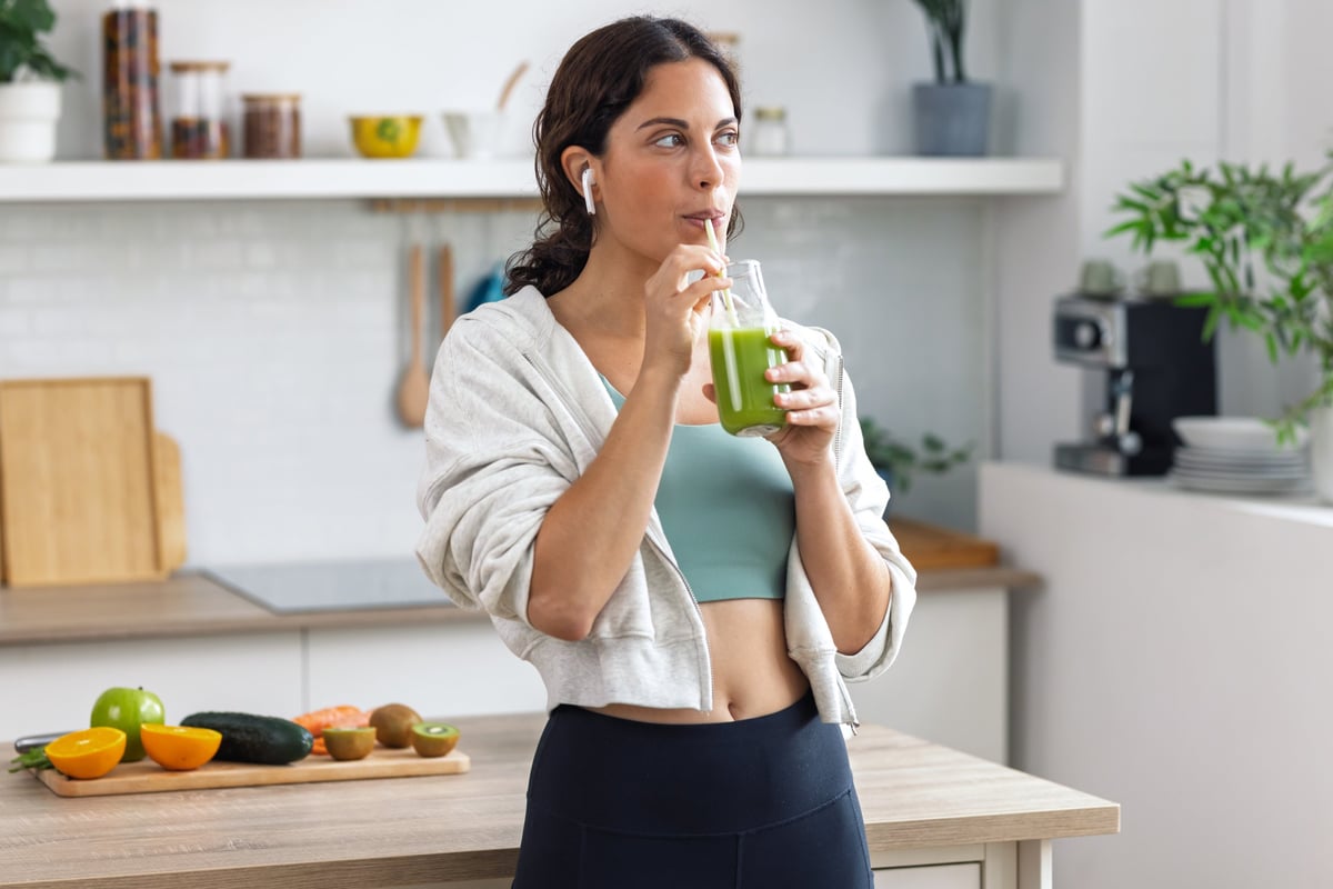 Sund og energisk kvinde der drikker en grøn smoothie i køkkenet – fokus på livsstil, kost og velvære